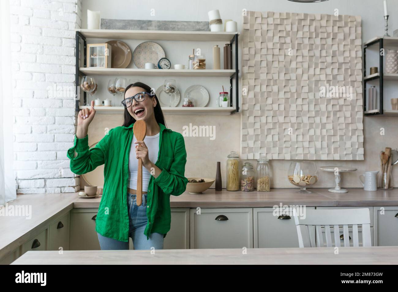 Gioiosa e felice giovane donna, casalinga, studente canta in cucina in un oggetto da cucina come un microfono e danze. Sta cucinando. Foto Stock