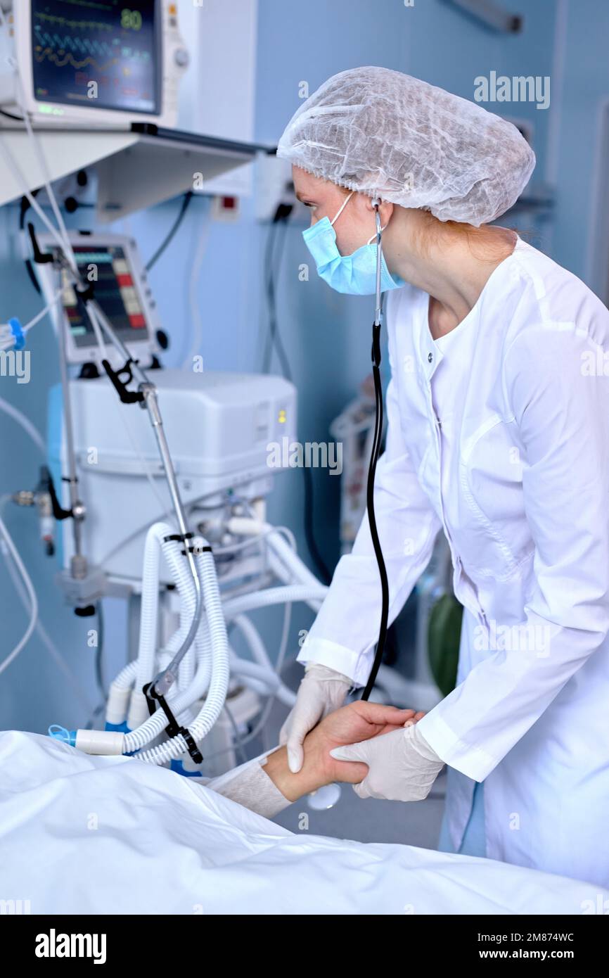 Medico caucasico esperto in Robe medico che verifica il polso del paziente sdraiato sul letto, tenendo la mano della persona malata. Nel moderno ospedale di Ward, Foto Stock