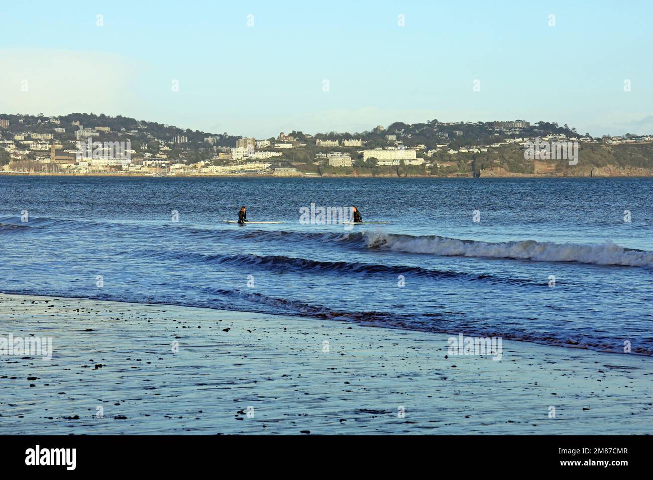 Due giovani donne in mute da surf in piccole onde vicino alla riva di Paignton, prese il 2023 gennaio. Inverno Foto Stock