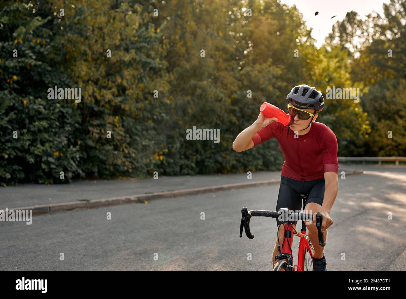 Ciclista sportiva professionale in casco nero, occhiali protettivi e  abbigliamento attivo in bicicletta dinamica acqua potabile per una maggiore  velocità. Uomo prepar Foto stock - Alamy