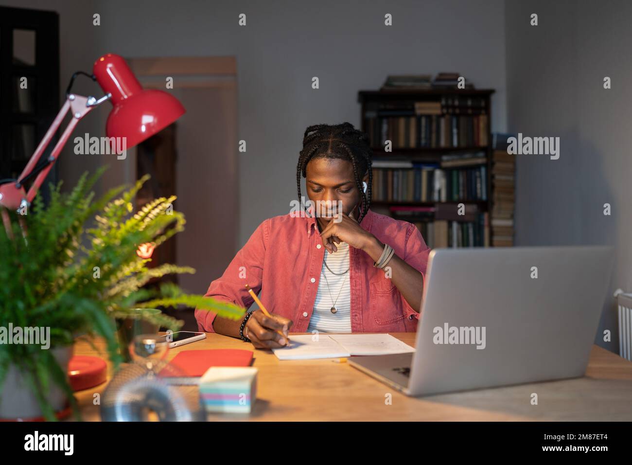 Puzzled giovane uomo nero fare nota touch chin lavoro su difficile progetto di ricerca utilizzare notebook alla scrivania. Foto Stock
