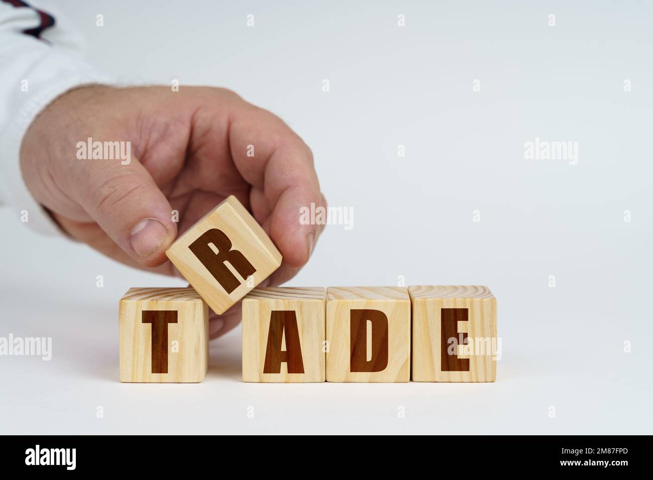 Concetto aziendale. Su una superficie bianca, un uomo impila cubi con l'iscrizione - COMMERCIO Foto Stock