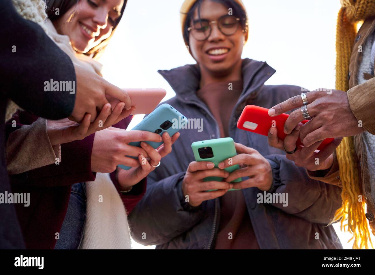 Quattro amici multirazziali che si riuniscono in cerchio utilizzando il telefono all'aperto. Foto Stock