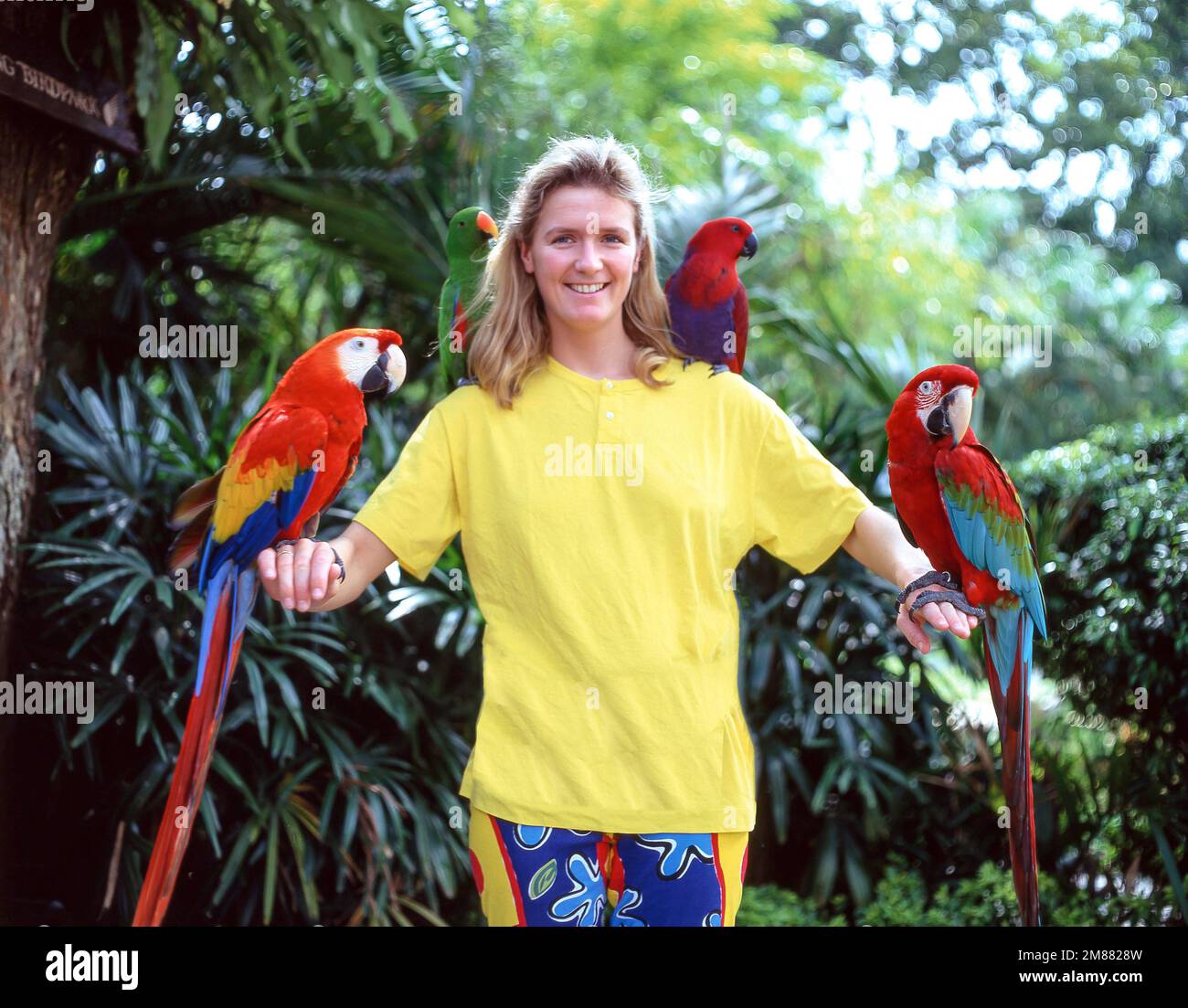Giovane donna turistica in posa con pappagalli Macaw, Jurong Bird Park, Jurong Hill, Singapore Island (Pulau Ujong), Singapore Foto Stock
