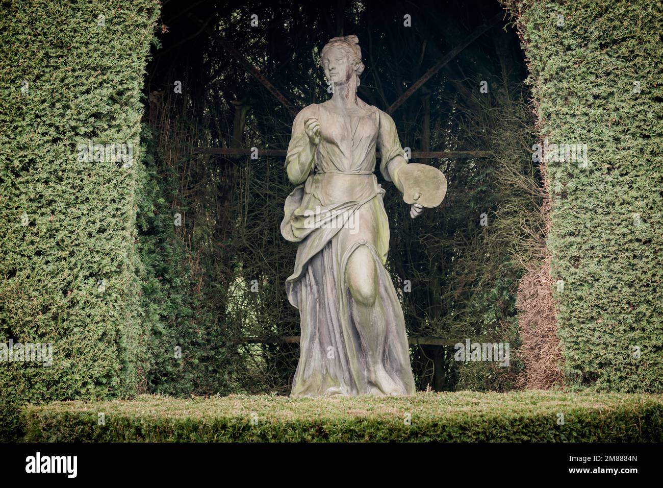 Statua di piombo di una musa che rappresenta le arti, qui pittura, con la tavolozza dell'artista e drappeggi in una rientranza di siepi presso Hardwick Hall, Derbyshire Foto Stock
