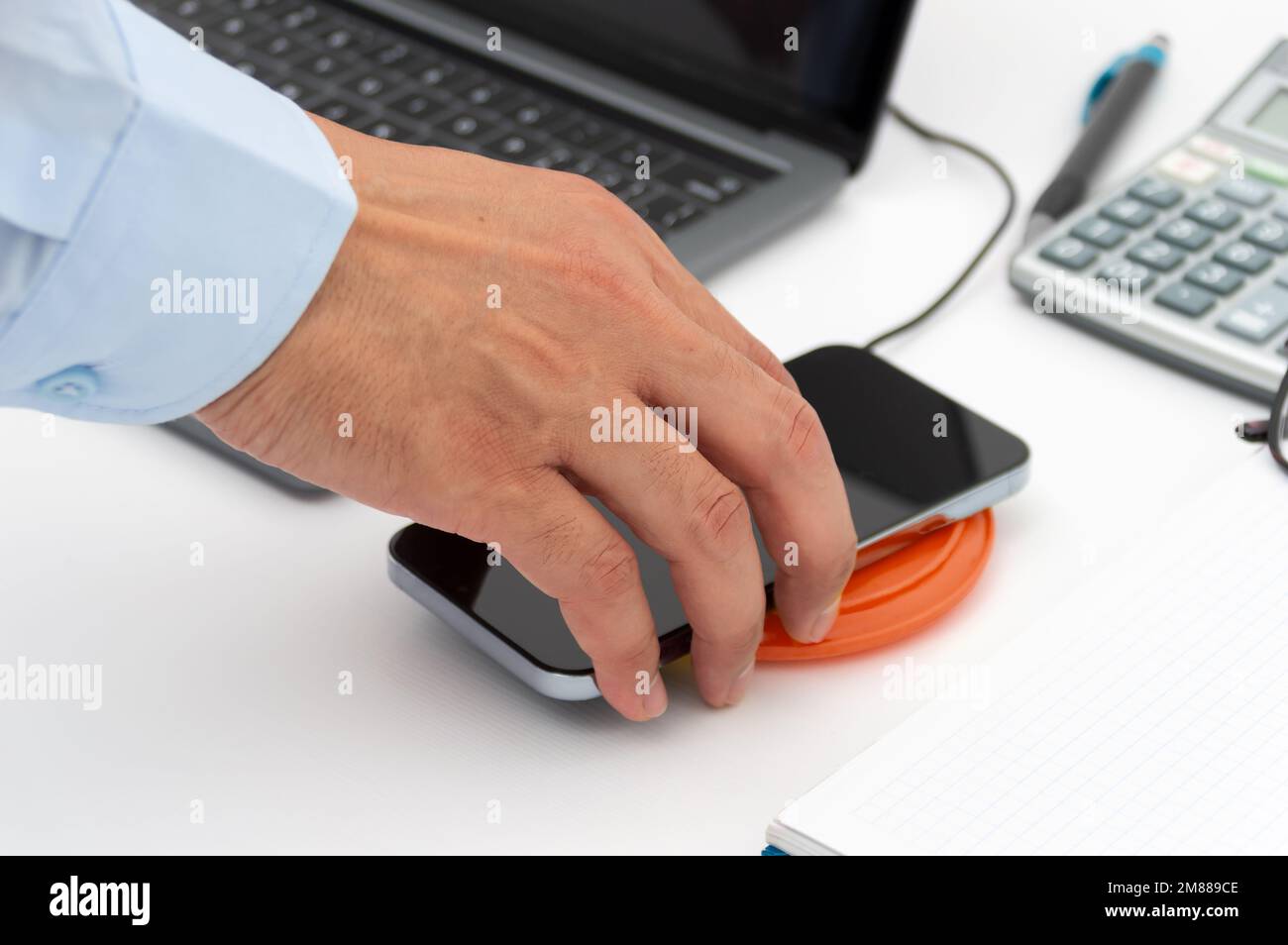 Mano di un uomo d'affari che carica il suo smartphone con un caricabatterie wireless in ufficio Foto Stock