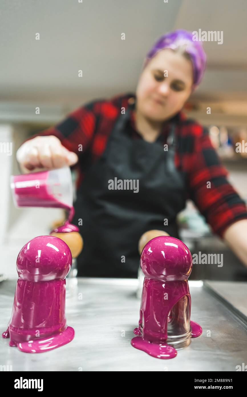 colpo verticale di un panettiere femminile dai capelli viola che mette la crema rosa sulle sfere di cioccolato. Foto di alta qualità Foto Stock