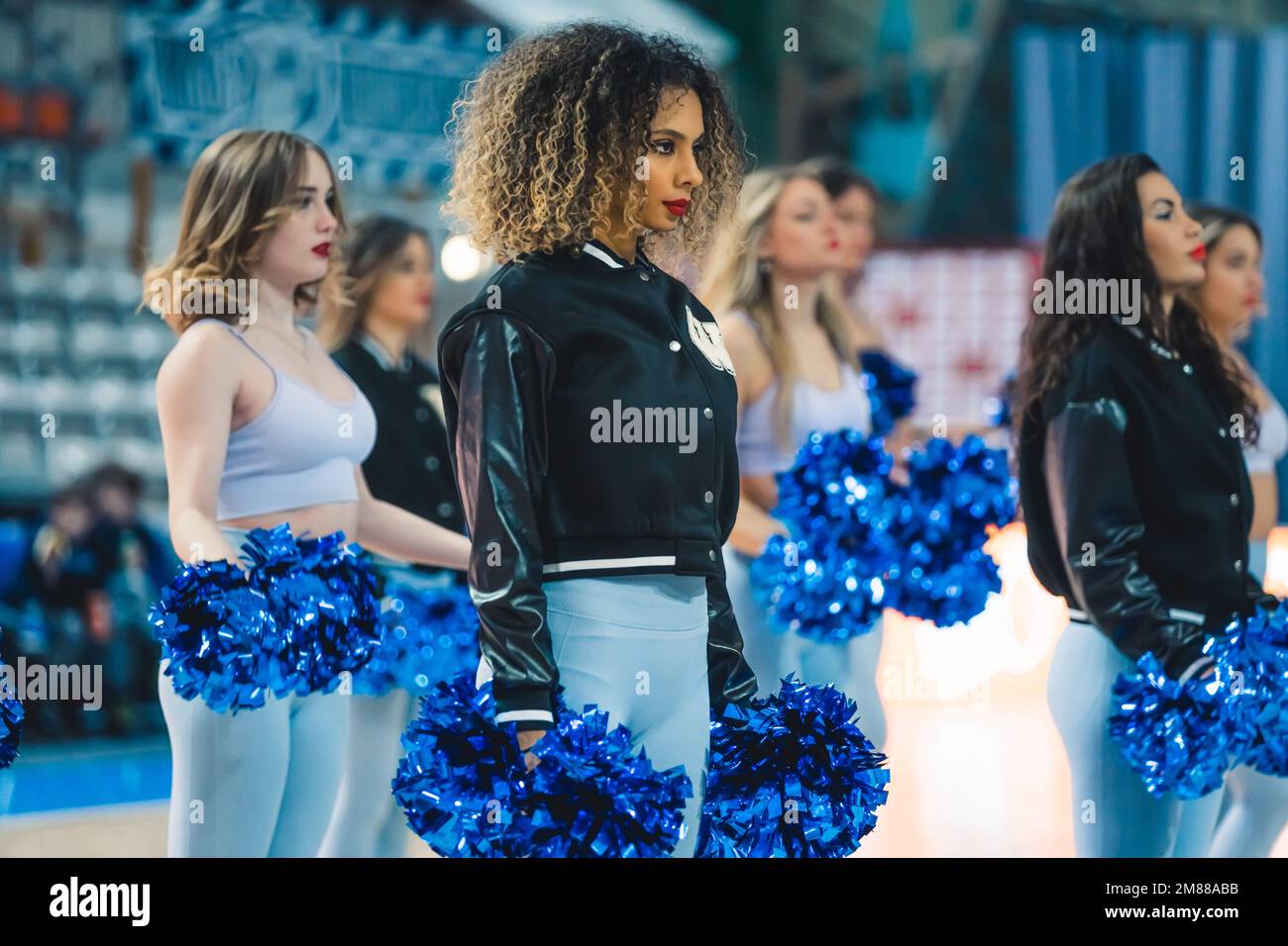 Un gruppo di cheerleaders multirazziali in uno stadio durante una partita. I cheerleaders stanno tenendo un paio di pom-pom blu nelle loro mani. Trasmette l'atletismo, lo spirito e il lavoro di squadra di cheerleader. Foto Stock