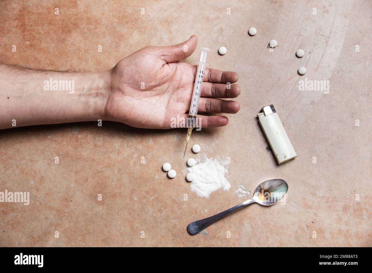 Primo piano shot di un braccio limp tossicodipendenti con farmaco paraphernalia che si trova accanto ad esso Foto Stock