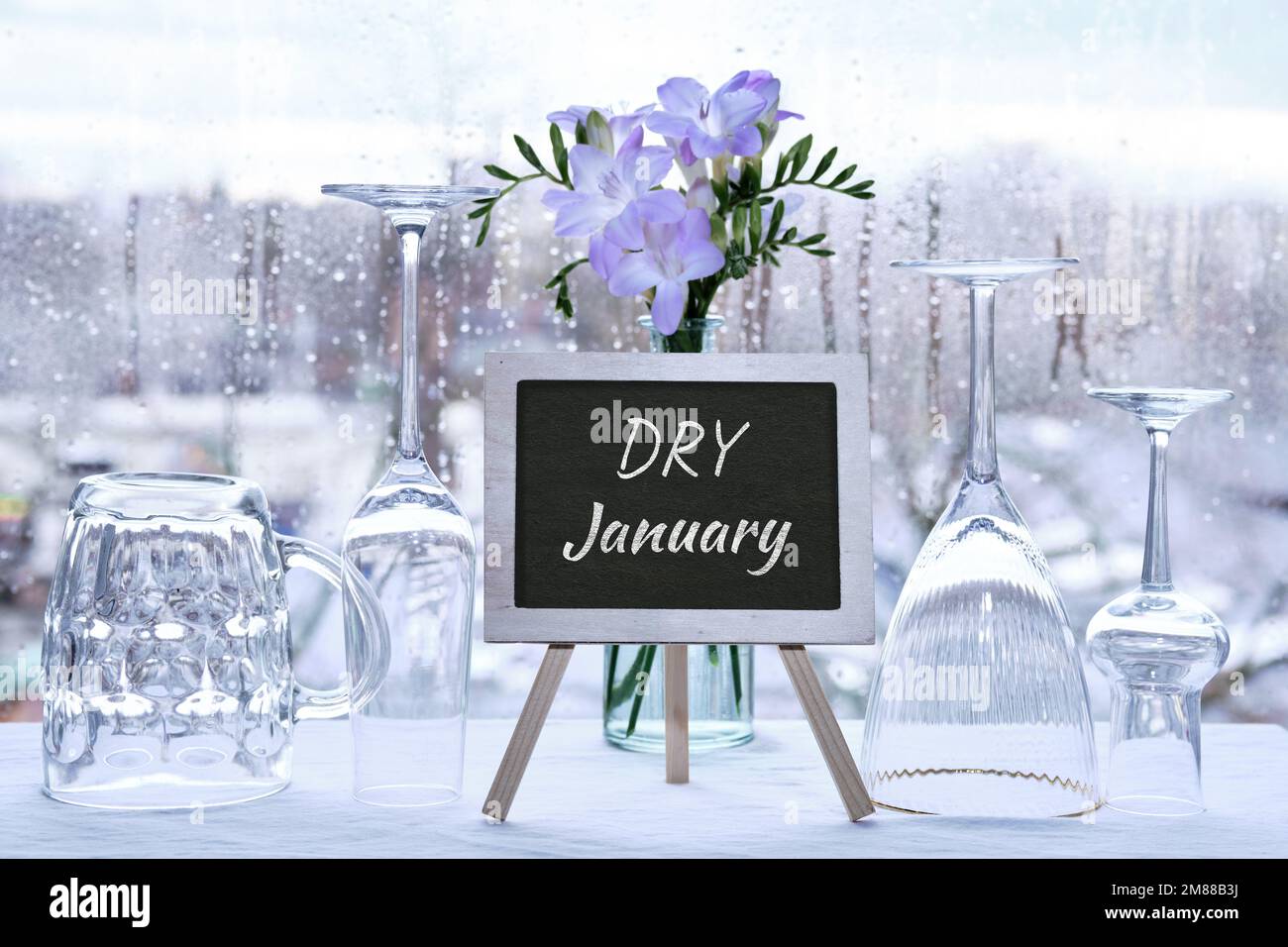 Gennaio secco, mese senza alcool. Testo Dry Gennaio su lavagna, lavagna a gesso. Vino vuoto e birra bicchieri da bere, fiori di freesia. Finestra con Foto Stock