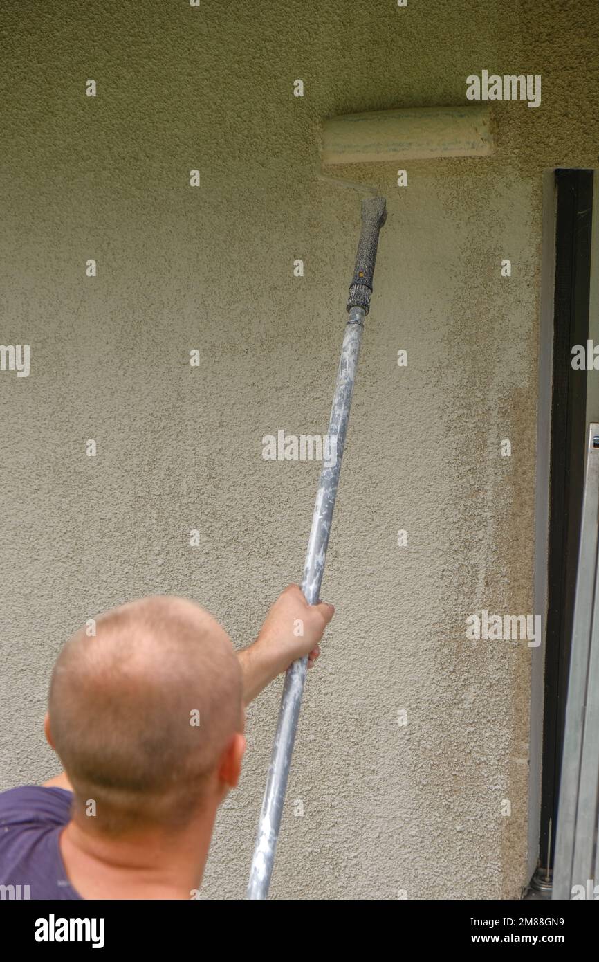 pittura di parete. L'uomo dipinge un muro a casa in beige con un lavoro Roller.Repair a home.Building, riparando e dipingendo una casa Foto Stock