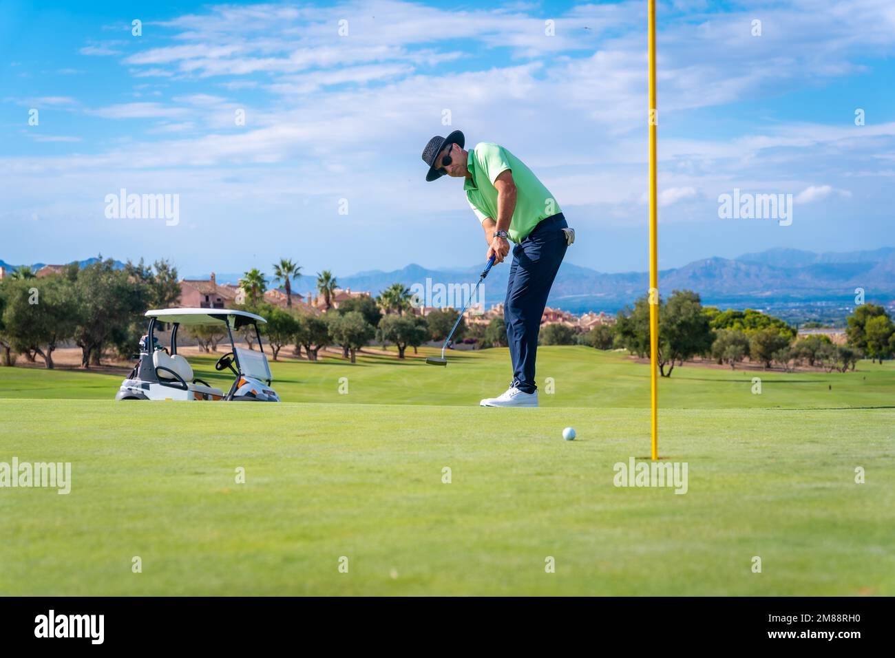 Uomo che gioca a golf, mettendo la palla nel buco sul verde con il putter Foto Stock