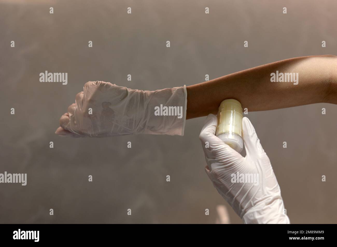 Tenere con guanti la mano e applicare una bottiglia di balsamo cosmetico in laboratorio Foto Stock