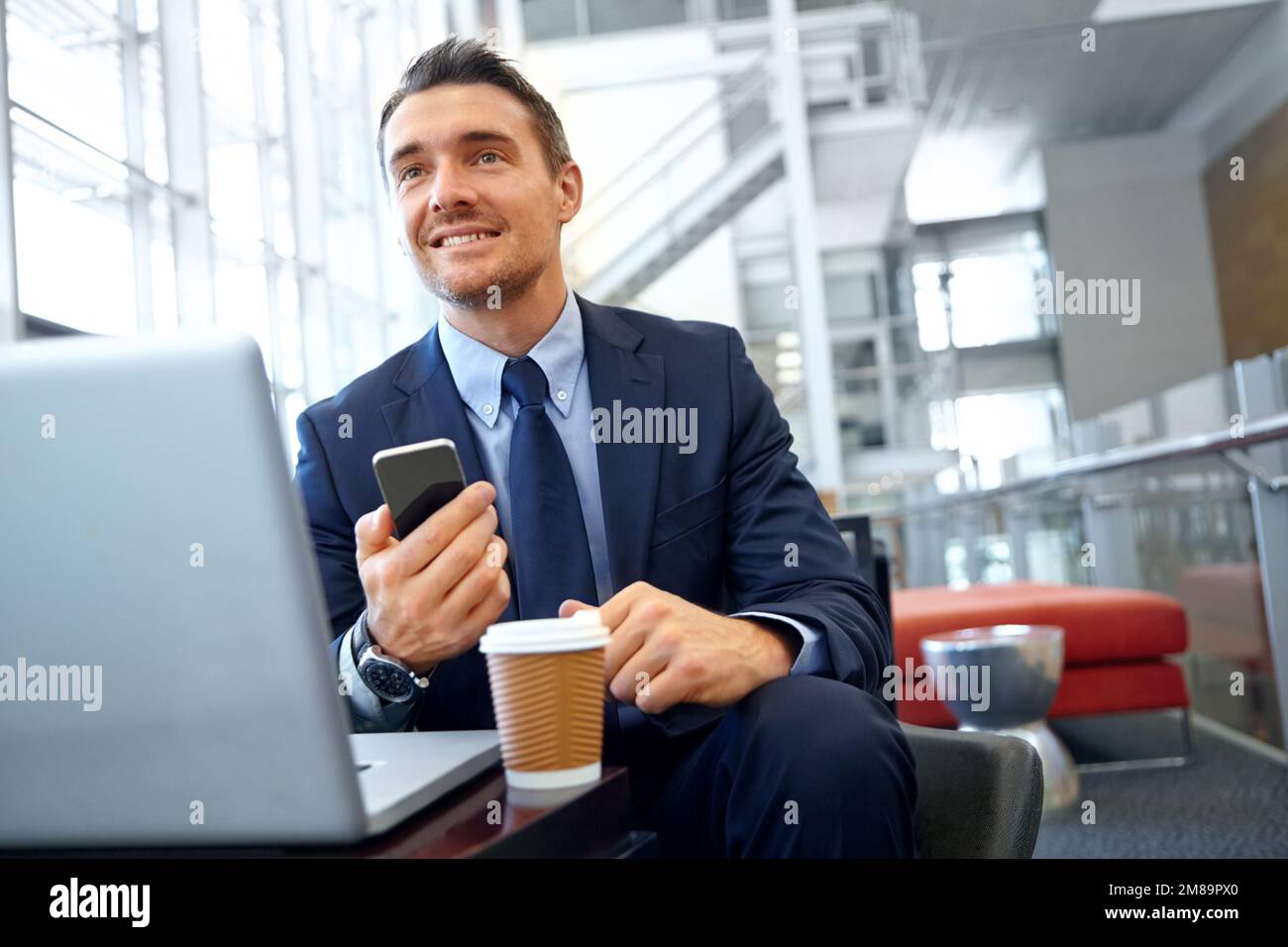 Uomo d'affari, smartphone e computer portatile in sala d'attesa aziendale, pensiero e marketing digitale. Startup, imprenditore maschile e ceo con cellulare, sociale Foto Stock