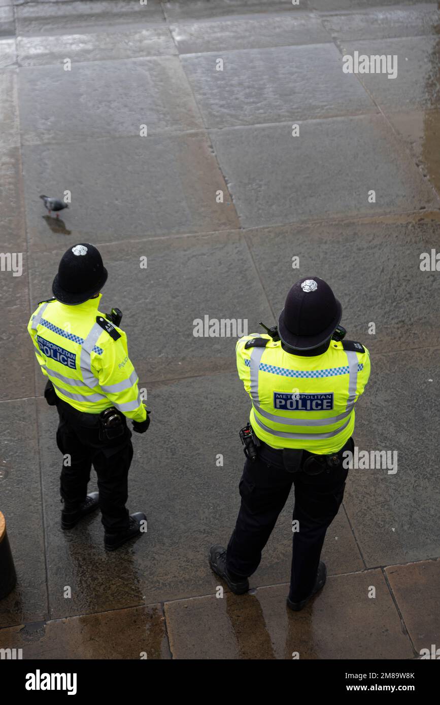 Pattugliamento della polizia metropolitana a Trafalgar Square, Westminster, Londra, Regno Unito, in una giornata invernale bagnata. Lastre per pavimentazione a umido Foto Stock