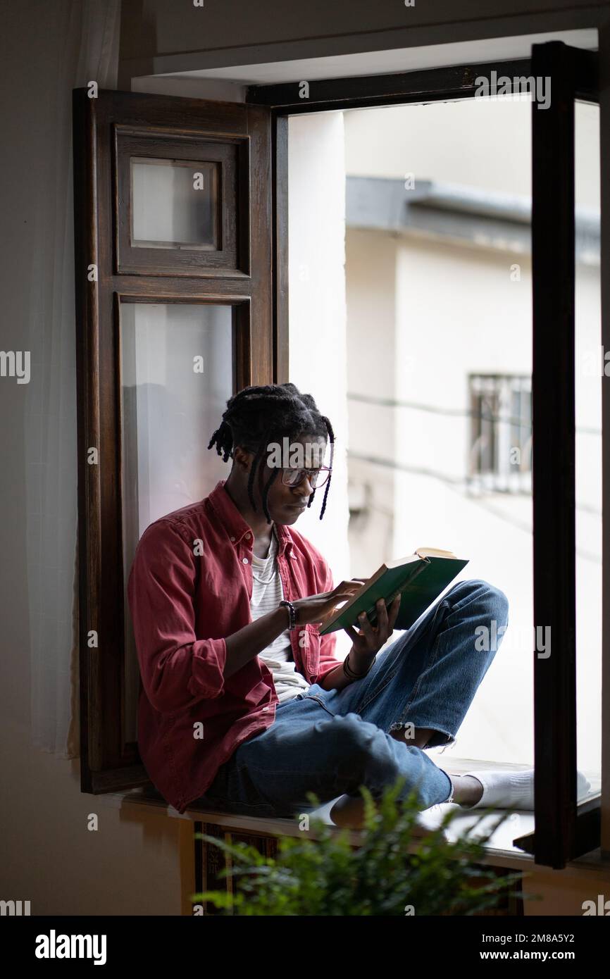 L'uomo nero sconvolto e eccitato dalla lettura siede sul davanzale con le preoccupazioni drammatiche del libro circa i caratteri. Foto Stock