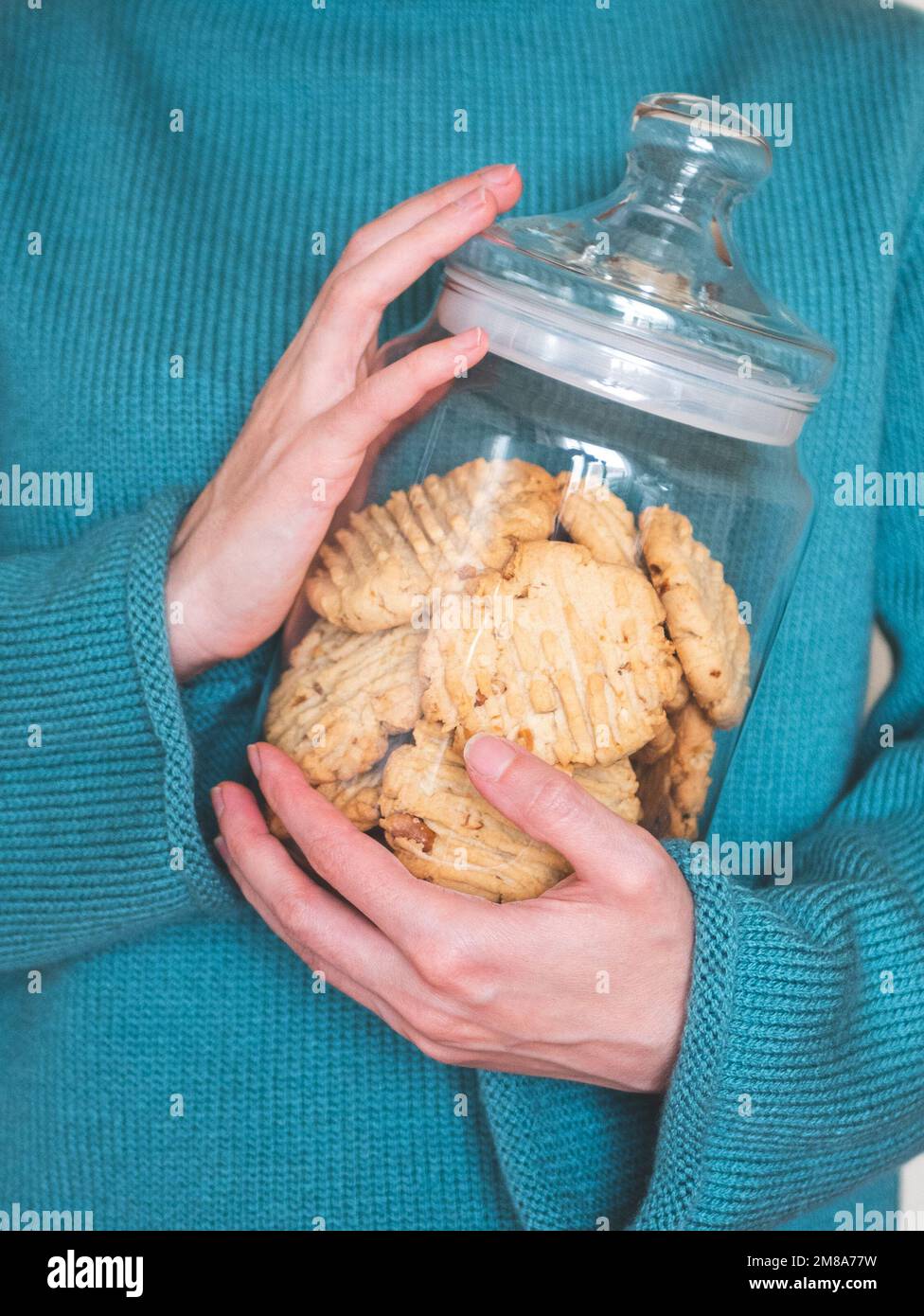 Vasetto di vetro con biscotti fatti in casa in mani umane, focus selettivo. Biscotti dolci, formato verticale Foto Stock