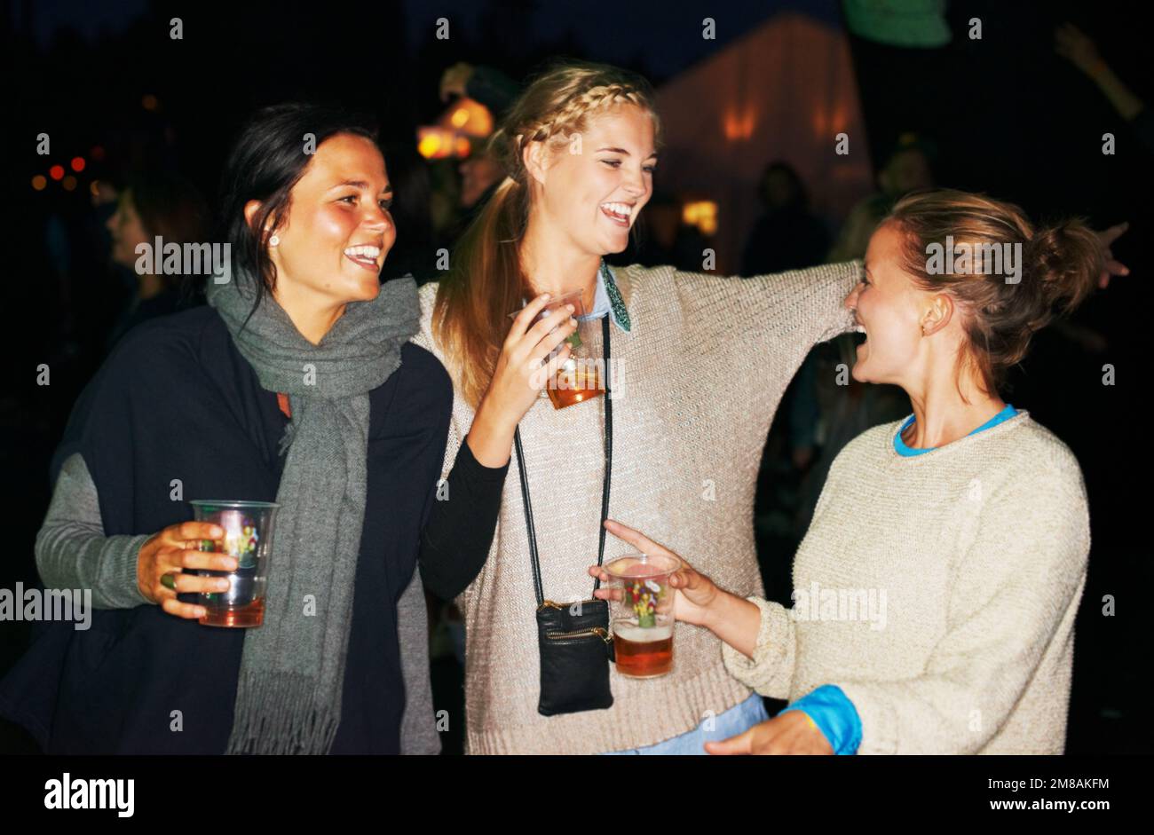 Giovani e non una cura nel mondo. tre amici che parlano e bevono di notte in un festival di musica all'aperto. Foto Stock