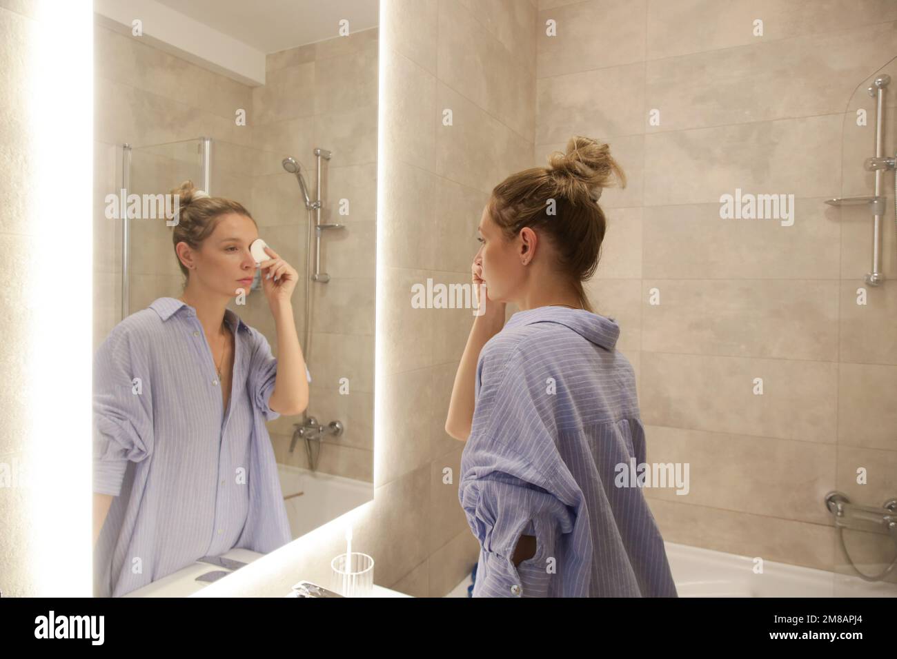 Giovane donna che fa la sua routine mattutina o serale nella parte anteriore dello specchio in bagno, igiene personale e concetto di bellezza Foto Stock