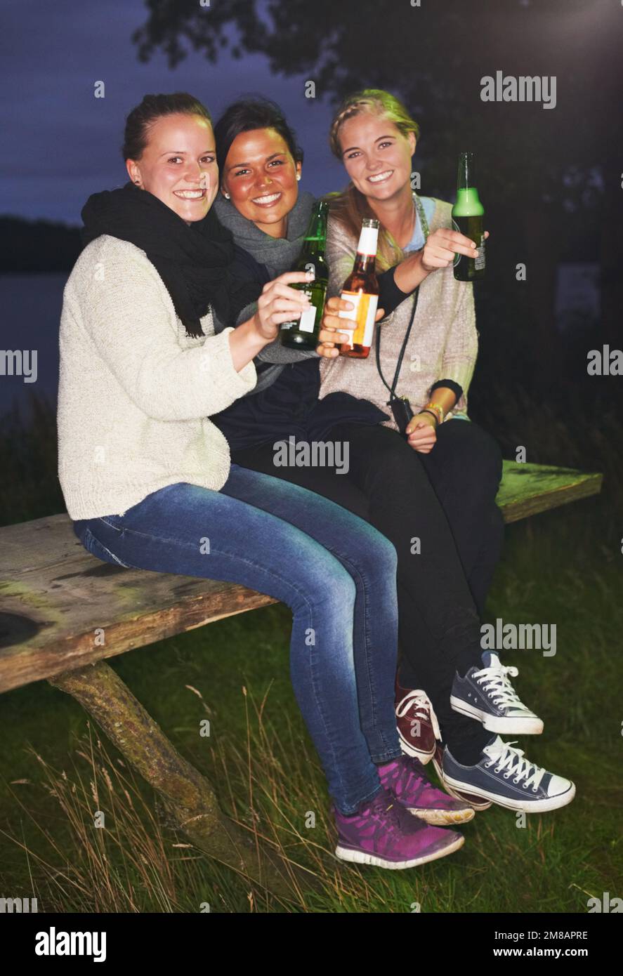 Bei momenti con gli amici. tre amici che parlano e bevono di notte in un festival di musica all'aperto. Foto Stock