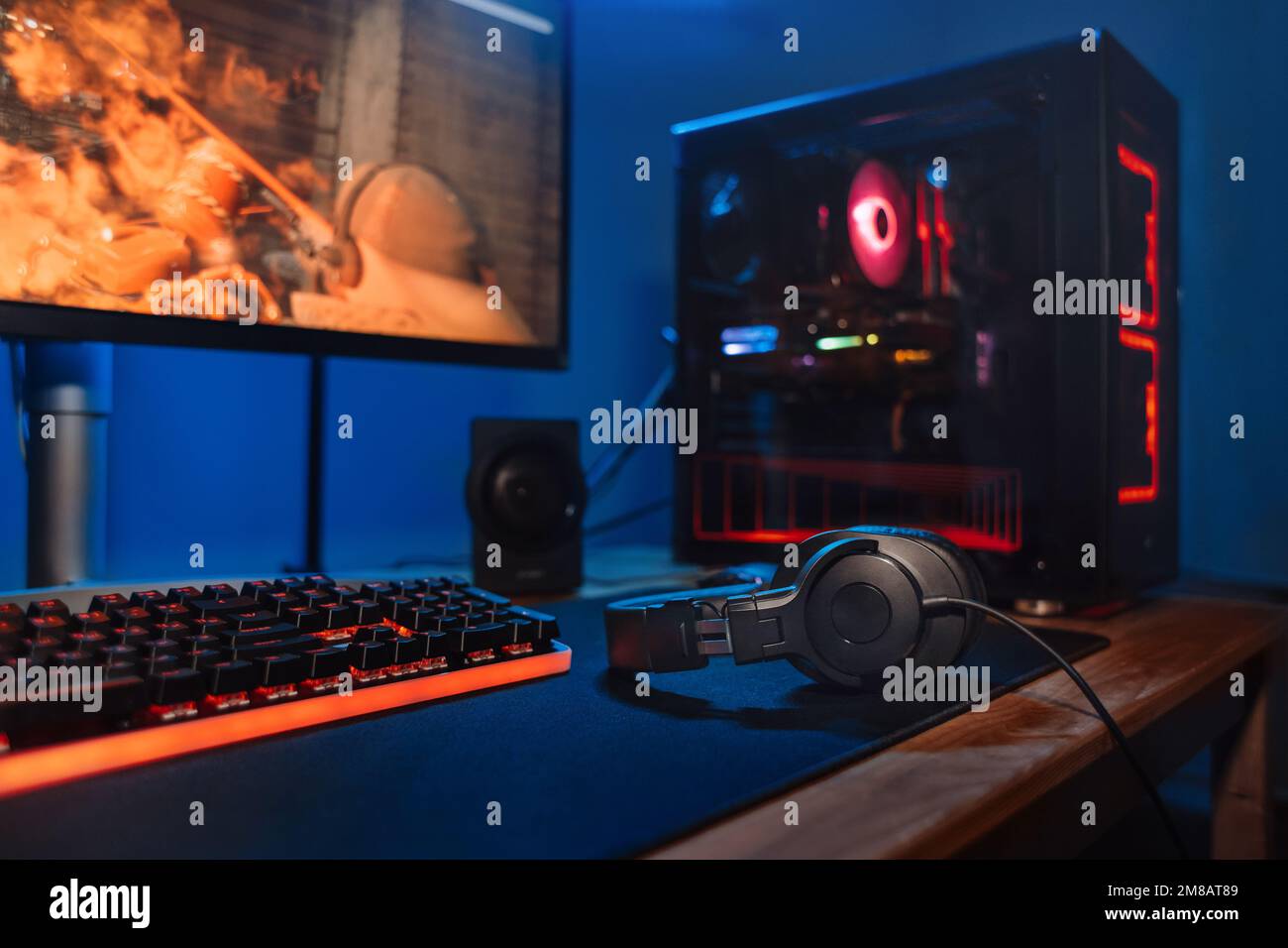 Ambiente di lavoro per i videogamer con nuova tastiera di gioco, mouse, cuffie, PC moderno con luce blu sfocata e rossa al neon. Potente personal computer per gamer di sport e cyber sul tavolo a casa. Primo piano Foto Stock