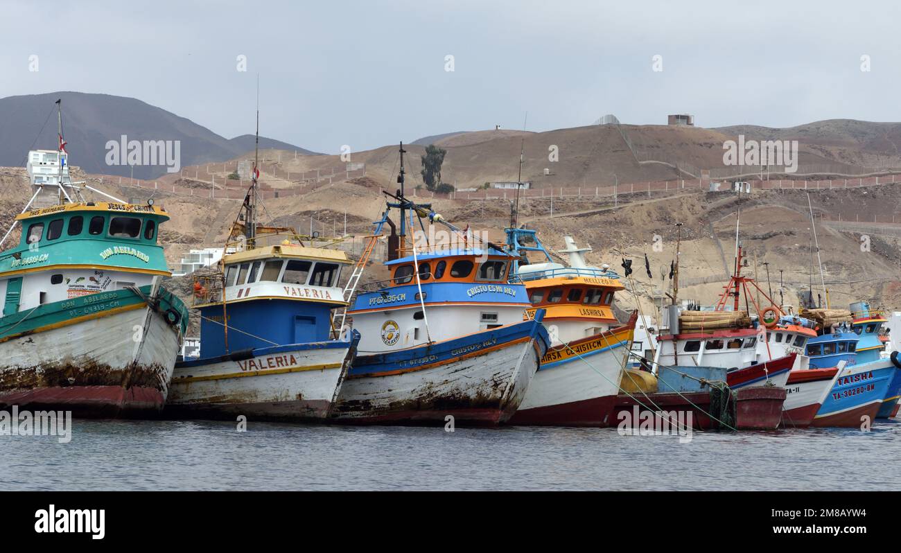 Barche da pesca ormeggiate nella baia di Pucusana con il paesaggio costiero deserto sullo sfondo. Pucusana, Lima, Perù Foto Stock