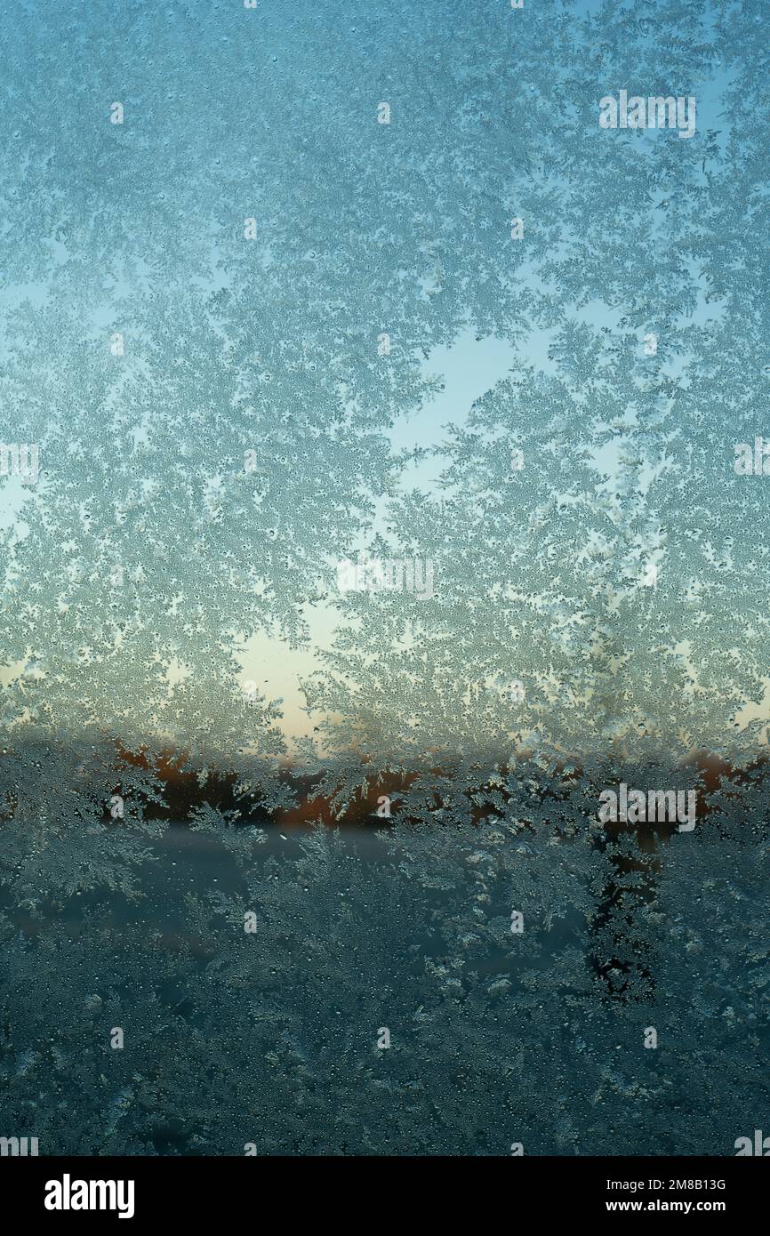 Schemi di congelamento sul vetro del vetro. Vetro smerigliato con cielo blu dietro. Delicati cristalli formati a basse temperature. Foto Stock