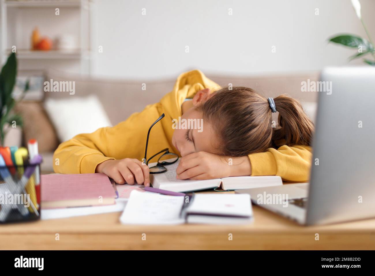 La ragazza della scuola esaurita che dorme alla scrivania mentre fa i lotti del lavoro, ottenendo pronta prima degli esami, sollecitata, è stata stanca dallo studiare, troppo imparare. Interni domestici. Homeschooling, formazione di distanza Foto Stock