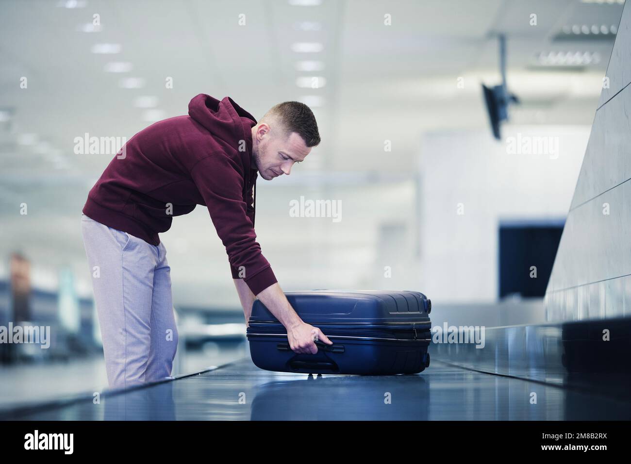 Viaggiare in aereo. Il passeggero ritira la sua valigia blu nel ritiro bagagli nel terminal dell'aeroporto. Foto Stock