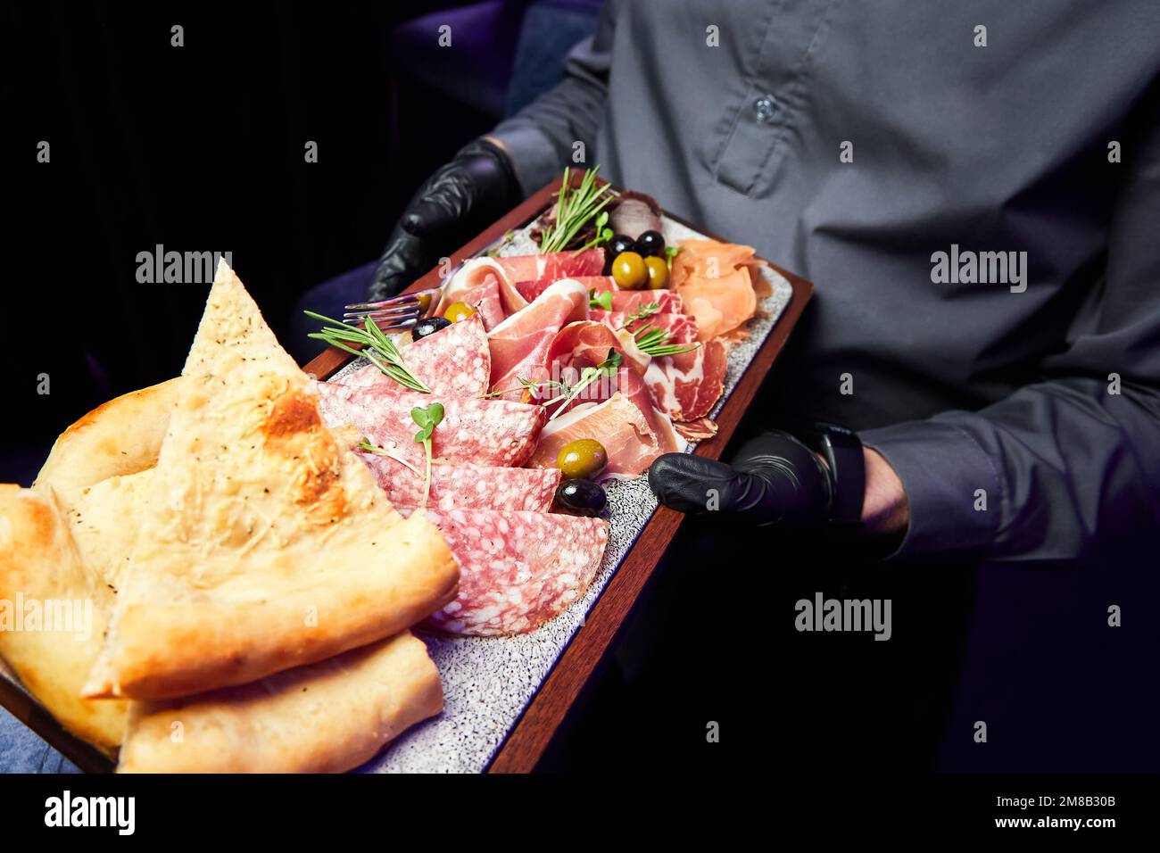 Il cameriere tiene un piatto di legno con varie prelibatezze secche a fette Foto Stock