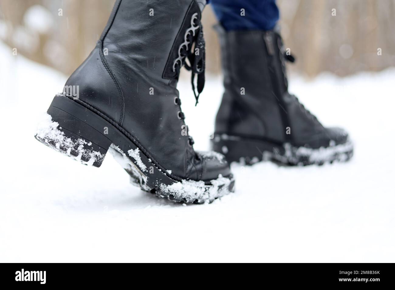 Gambe femminili in pelle nera stivali con lacci sulla neve. Donna che cammina sulla strada d'inverno, scarpe calde per il tempo freddo Foto Stock
