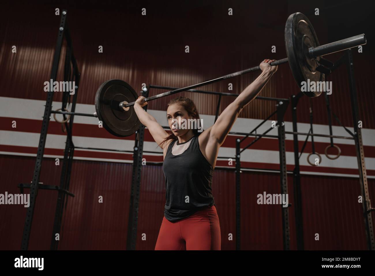 Giovane donna muscolosa che fa esercizi di sollevamento pesi alla palestra crossfit. Adatta l'atleta femminile sollevando pesi pesanti in palestra. Foto Stock