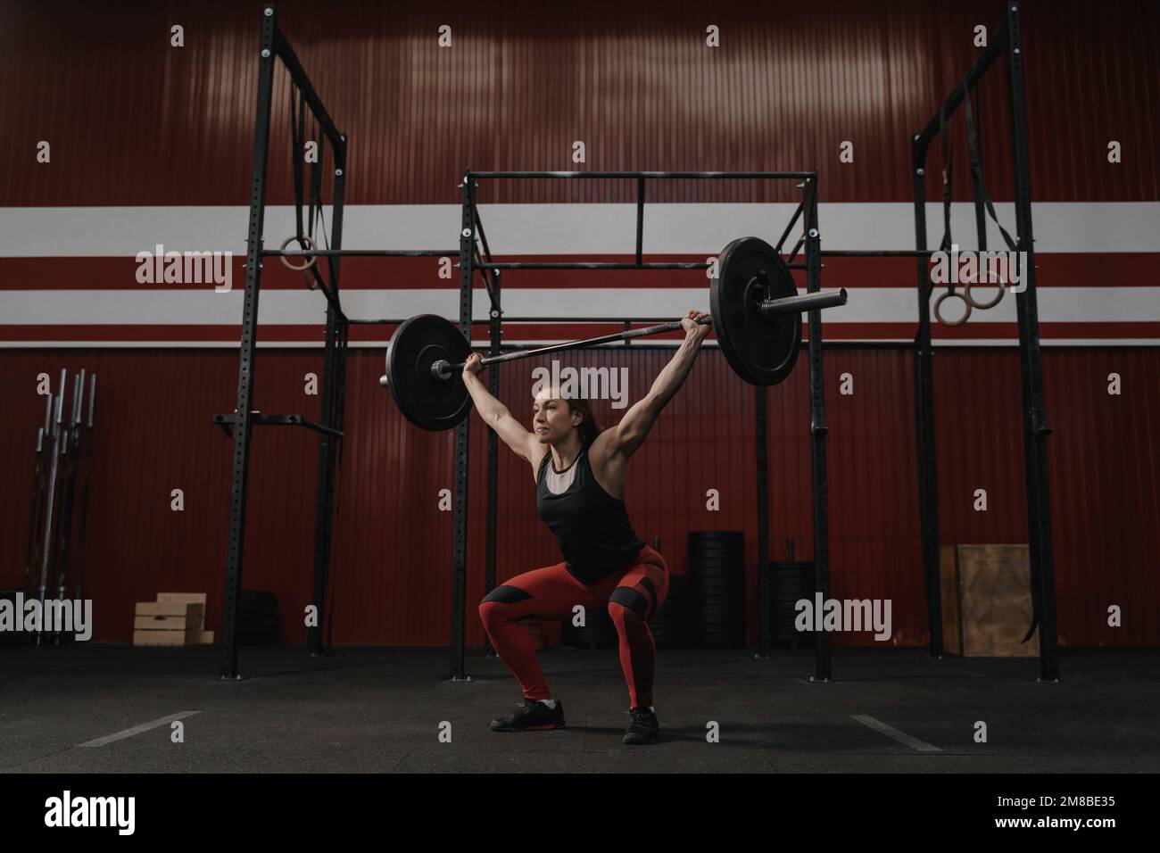 Donna forte che solleva il tetto del barbell, facendo le esercitazioni di crossfit. Adatta la giovane donna che solleva pesi pesanti in palestra. Foto Stock