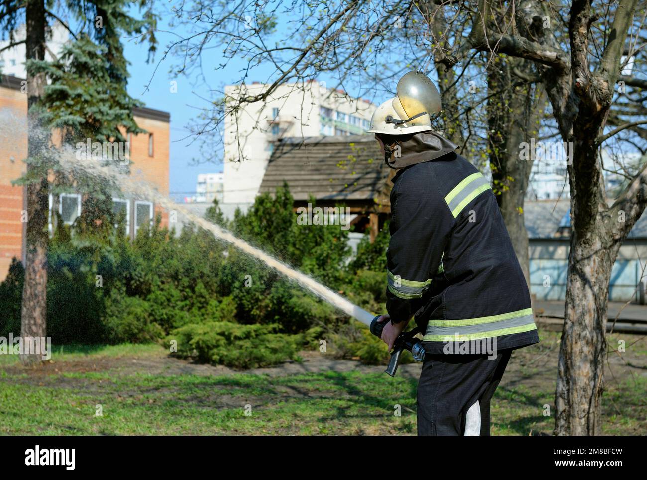 Pompieri in costume protettivo innaffiatura territorio con siringa, addestramento antincendio. Foto Stock