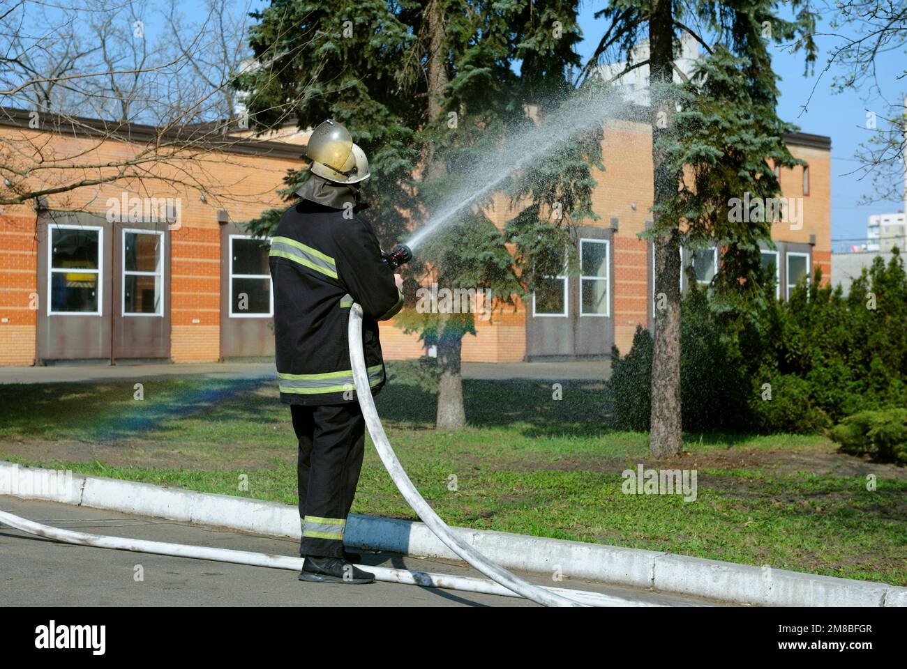 Pompieri in costume protettivo innaffiatura territorio con siringa, addestramento antincendio. Foto Stock