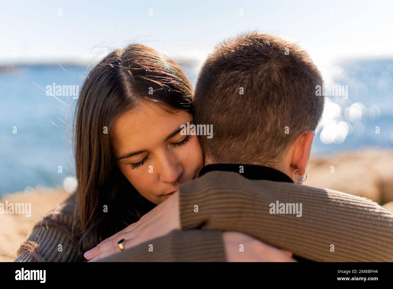 Giovane donna con occhi chiusi che abbraccia il ragazzo su sfondo sfocato del mare durante la celebrazione di San Valentino Foto Stock