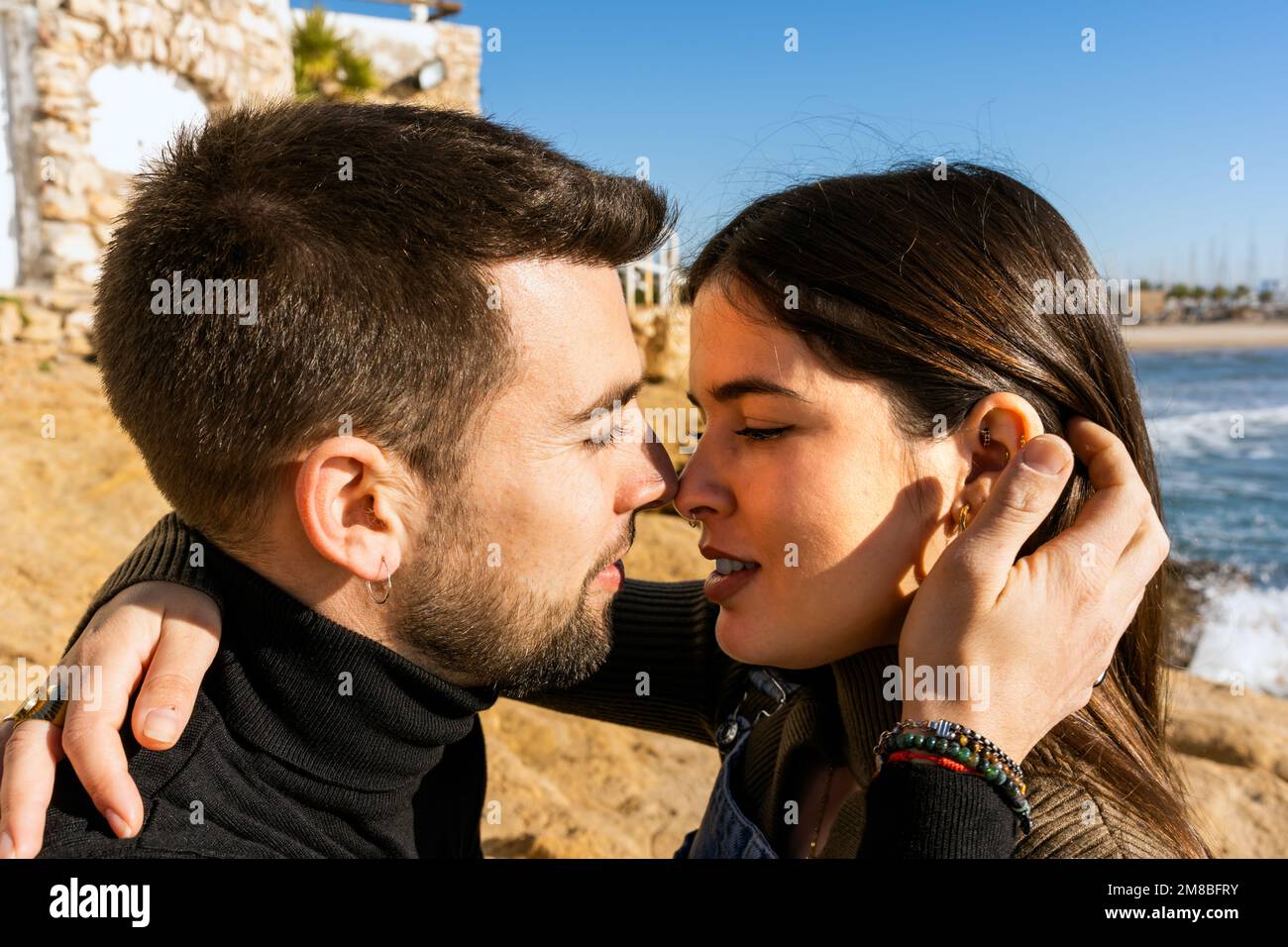 Giovane uomo che tocca i capelli e bacia la ragazza durante la romantica riva del mare ondeggiante il giorno di San Valentino Foto Stock
