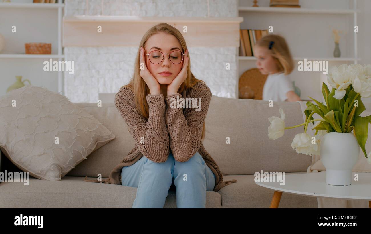 Stanco sconvolto madre caucasica seduta sul divano a casa triste frustrato stressato stressato stanchezza mamma soffrono mal di testa con rumore attivo difficile bambino Foto Stock