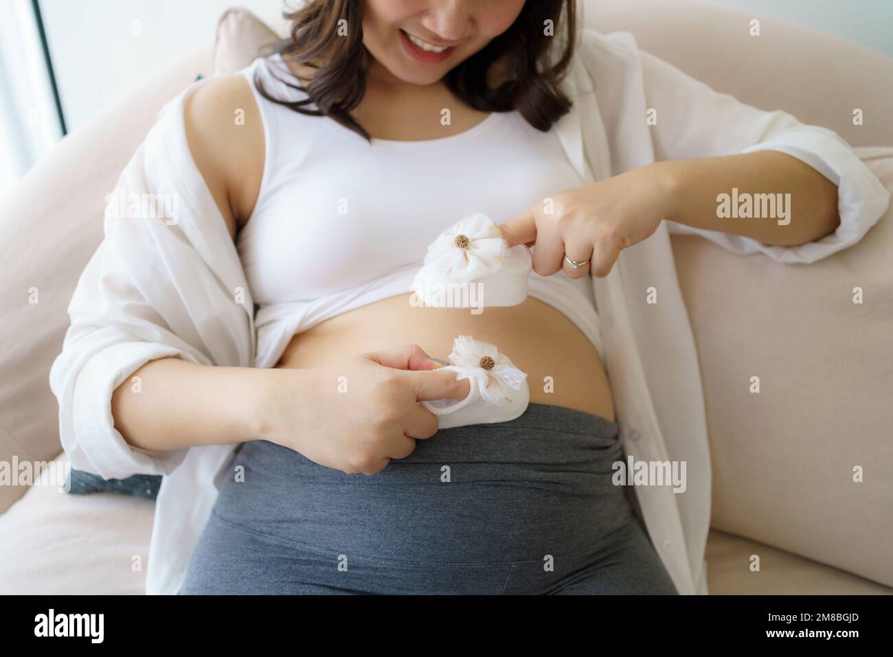 Donna asiatica incinta sentirsi felice a casa mentre si prende cura del suo bambino. La giovane madre in attesa che tiene il bambino nel ventre incinta. Maternità prenat Foto Stock