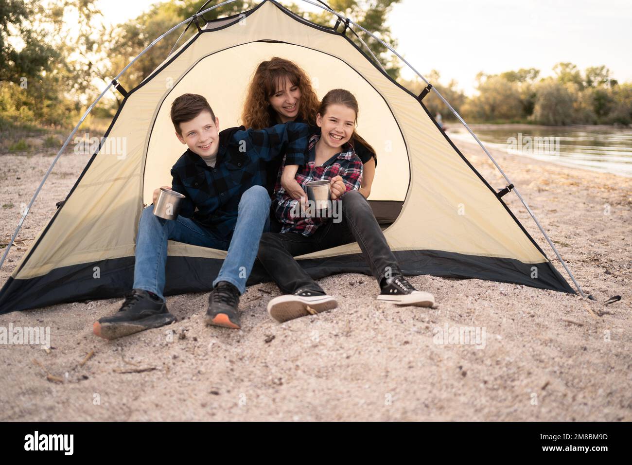 Ritratto di famiglia di viaggiatori in tenda guardando la fotocamera. sorridendo madre, ragazza e ragazzo che si guarda felice fuori dalla tenda. Esplorare la natura su autu famiglia Foto Stock