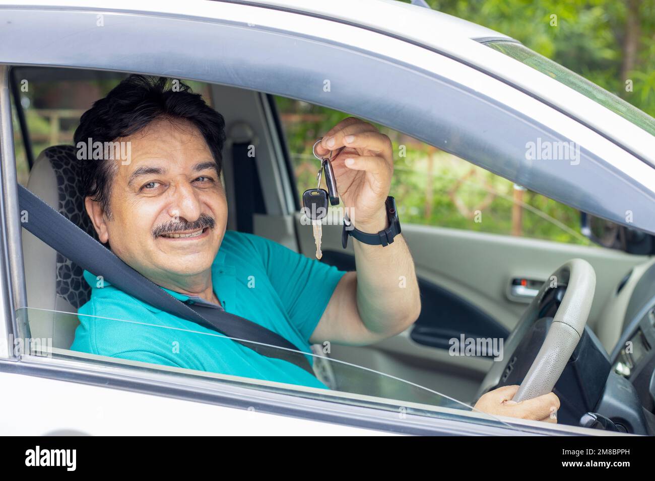 Uomo maturo indiano felice seduto in auto che indossa la cintura di sicurezza mostra la chiave con la mano pronta a guidare. È sufficiente acquistare un nuovo veicolo Foto Stock