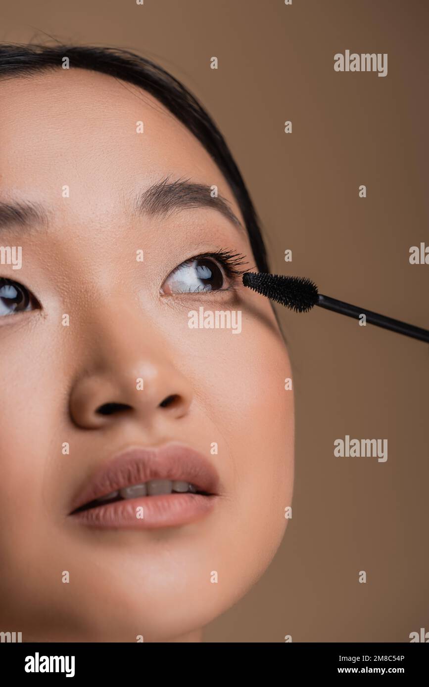 Vista ritagliata della donna asiatica con il trucco tenendo l'applicatore  mascara isolato su marrone, immagine stock Foto stock - Alamy