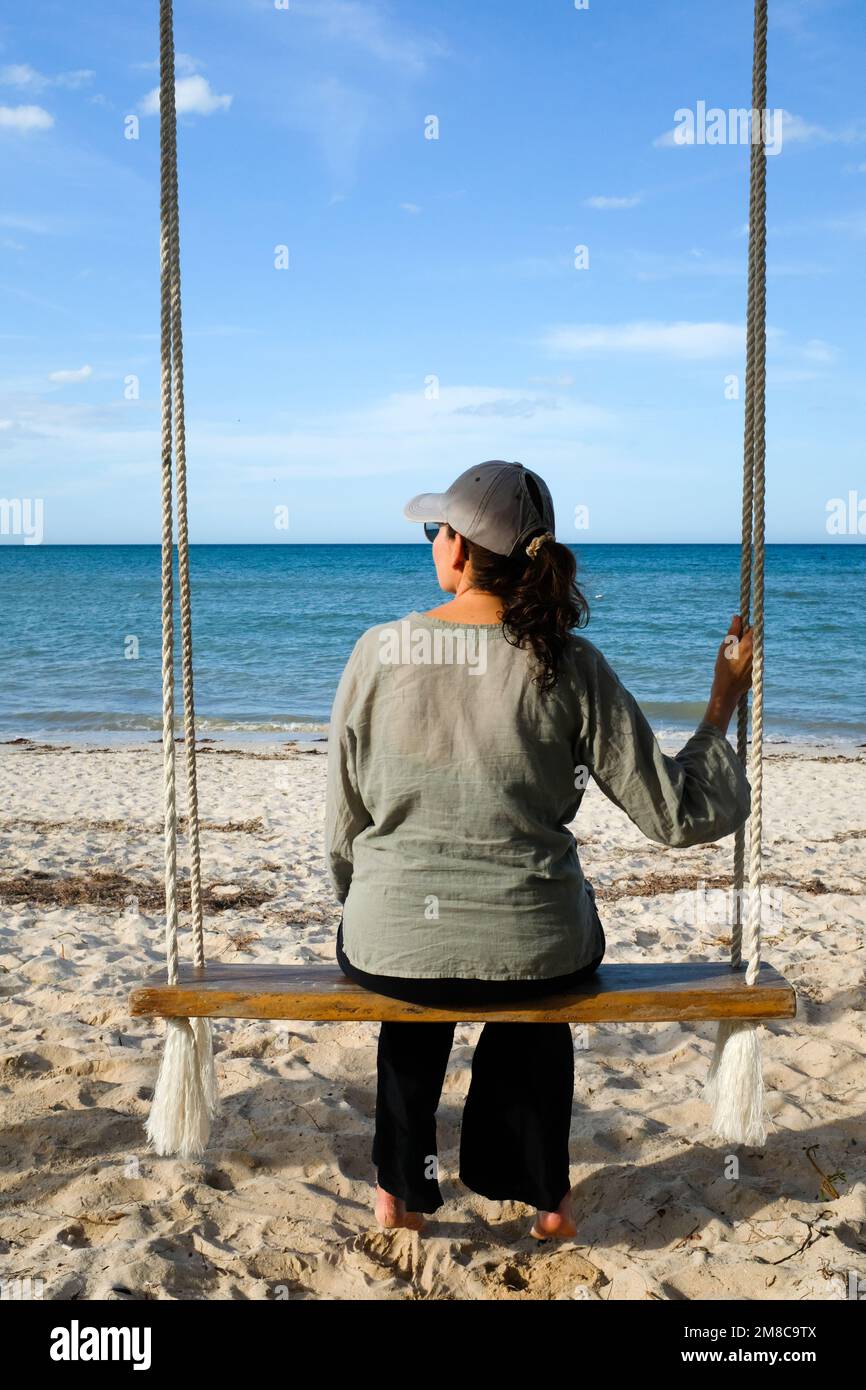 Donna seduta su una oscillazione in spiaggia Foto Stock