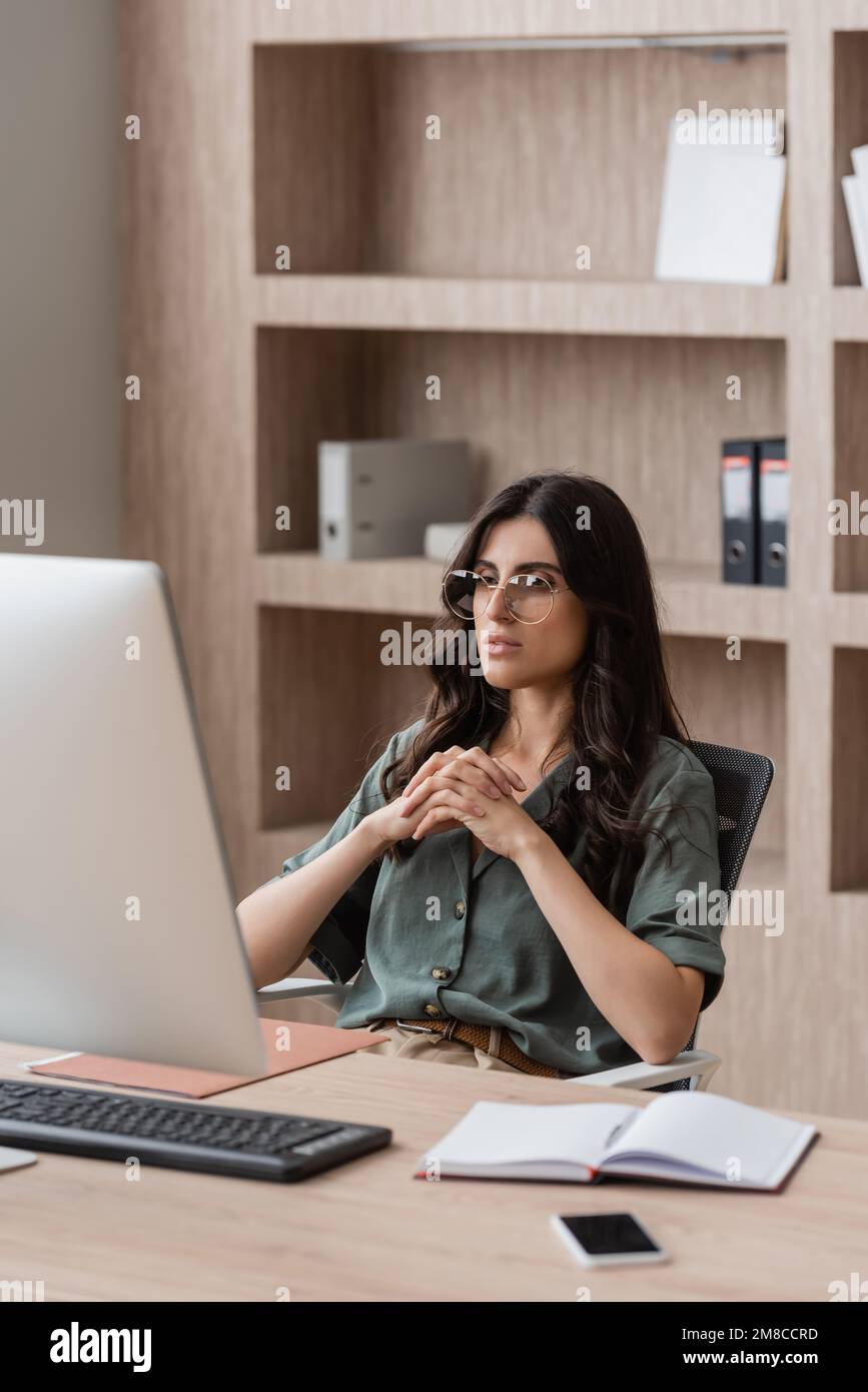 responsabile attento negli occhiali che guardano il monitor del computer vicino al notebook vuoto e al telefono cellulare sulla scrivania, immagine di scorta Foto Stock