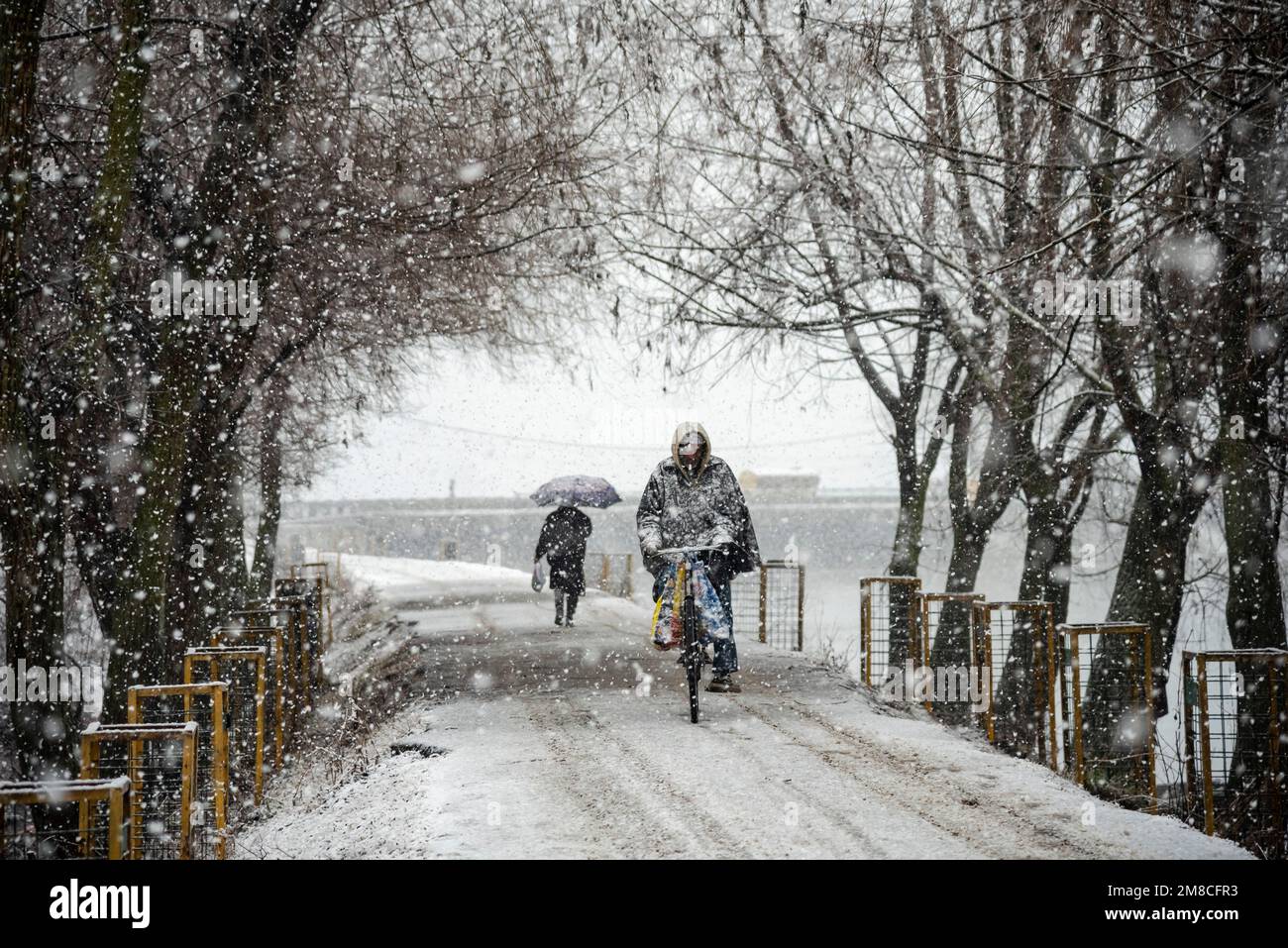 Un uomo passa in bicicletta davanti a un uomo che cammina lungo una strada coperta di neve durante le nevicate. Il Kashmir ha ricevuto nevicate fresche, con le cali più alte della valle che hanno ricevuto nevicate da moderate a pesanti e nevicate da leggere a moderate in pianura, causando una visibilità distruttiva. Questo ha influito sulle operazioni di volo insieme alla chiusura dell'autostrada nazionale Srinagar-Jammu. Foto Stock