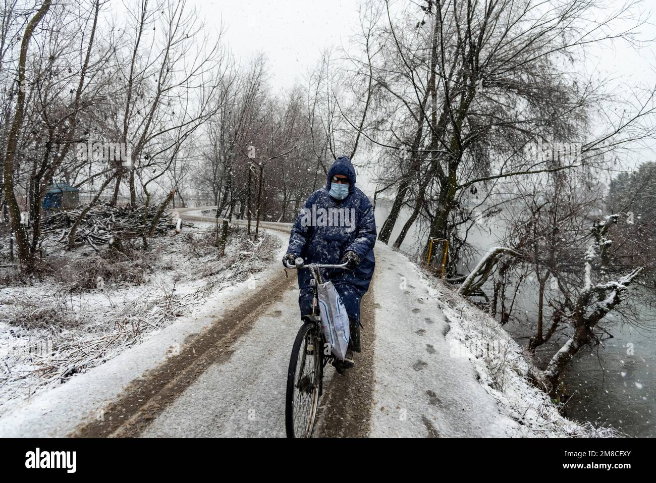 Un uomo guarda su mentre guida una bicicletta lungo una strada coperta di neve durante la caduta di neve. Il Kashmir ha ricevuto nevicate fresche, con le cali più alte della valle che hanno ricevuto nevicate da moderate a pesanti e nevicate da leggere a moderate in pianura, causando una visibilità distruttiva. Questo ha influito sulle operazioni di volo insieme alla chiusura dell'autostrada nazionale Srinagar-Jammu. Foto Stock