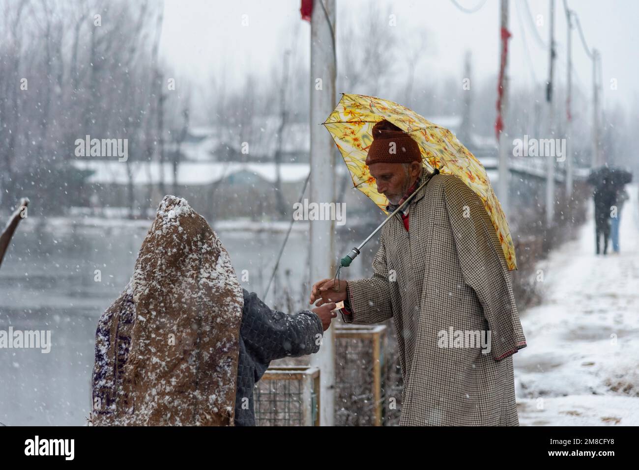 Un uomo con un ombrello trattare con il venditore di strada in caso di nevicate. Il Kashmir ha ricevuto nevicate fresche, con le cali più alte della valle che hanno ricevuto nevicate da moderate a pesanti e nevicate da leggere a moderate in pianura, causando una visibilità distruttiva. Questo ha influito sulle operazioni di volo insieme alla chiusura dell'autostrada nazionale Srinagar-Jammu. Foto Stock