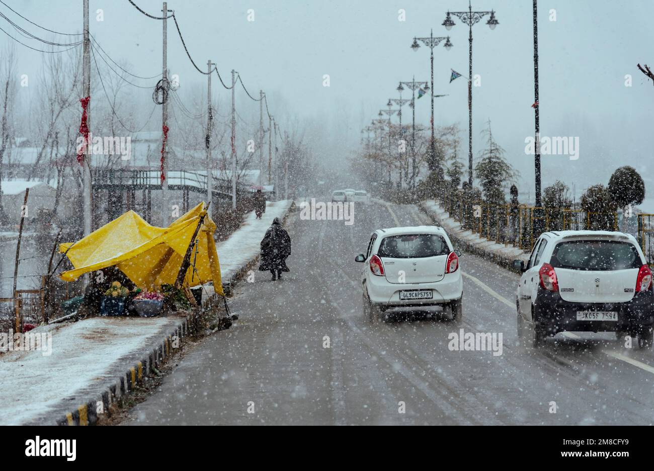 Un uomo cammina oltre del venditore di lato della strada durante la nevicata. Il Kashmir ha ricevuto nevicate fresche, con le cali più alte della valle che hanno ricevuto nevicate da moderate a pesanti e nevicate da leggere a moderate in pianura, causando una visibilità distruttiva. Questo ha influito sulle operazioni di volo insieme alla chiusura dell'autostrada nazionale Srinagar-Jammu. Foto Stock