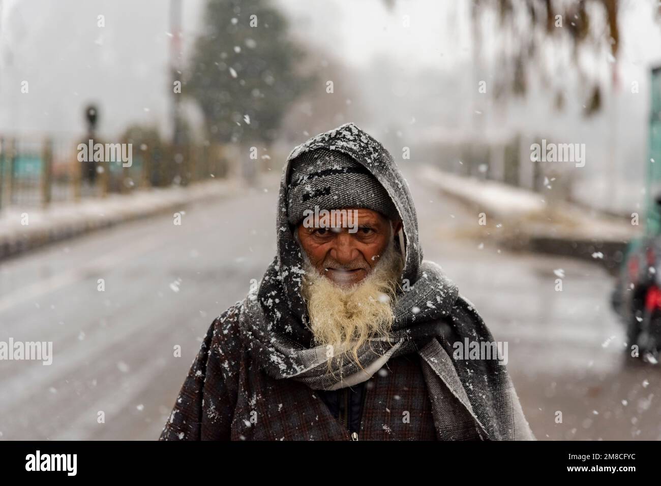 Un uomo anziano guarda mentre cammina in mezzo alla nevicata. Il Kashmir ha ricevuto nevicate fresche, con le cali più alte della valle che hanno ricevuto nevicate da moderate a pesanti e nevicate da leggere a moderate in pianura, causando una visibilità distruttiva. Questo ha influito sulle operazioni di volo insieme alla chiusura dell'autostrada nazionale Srinagar-Jammu. Foto Stock