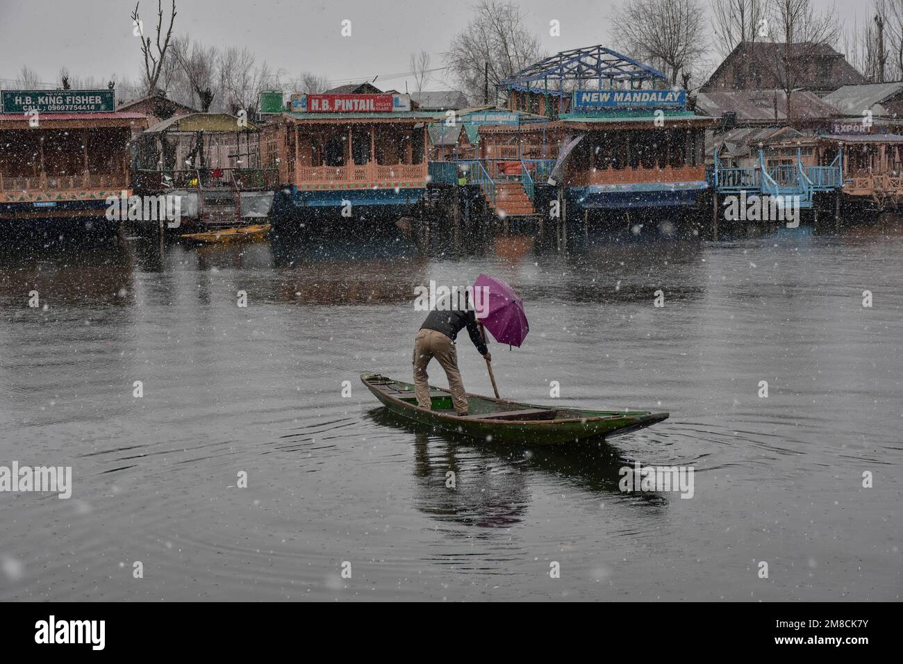 Un uomo tiene un ombrello mentre lotta per fare la fila della sua barca durante la nevicata. Parti della valle di Kashmir compreso Srinagar ha ricevuto nevicate che portano alla chiusura della vitale Srinagar-Jammu autostrada nazionale e la cancellazione delle operazioni di volo, funzionari qui ha detto. Foto Stock
